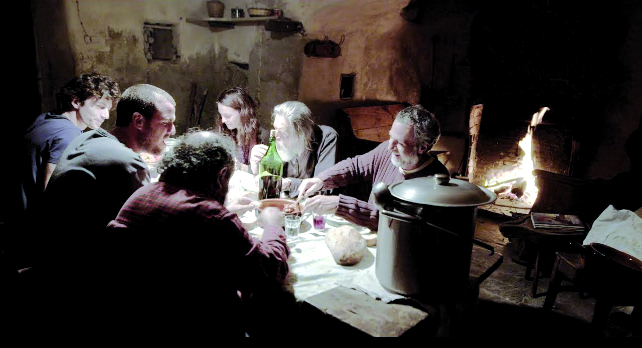Una scena del film "La terra buona" che ritrae un gruppo di persone che mangiano seduti ad una tavola comune in una vecchia baita di montagna